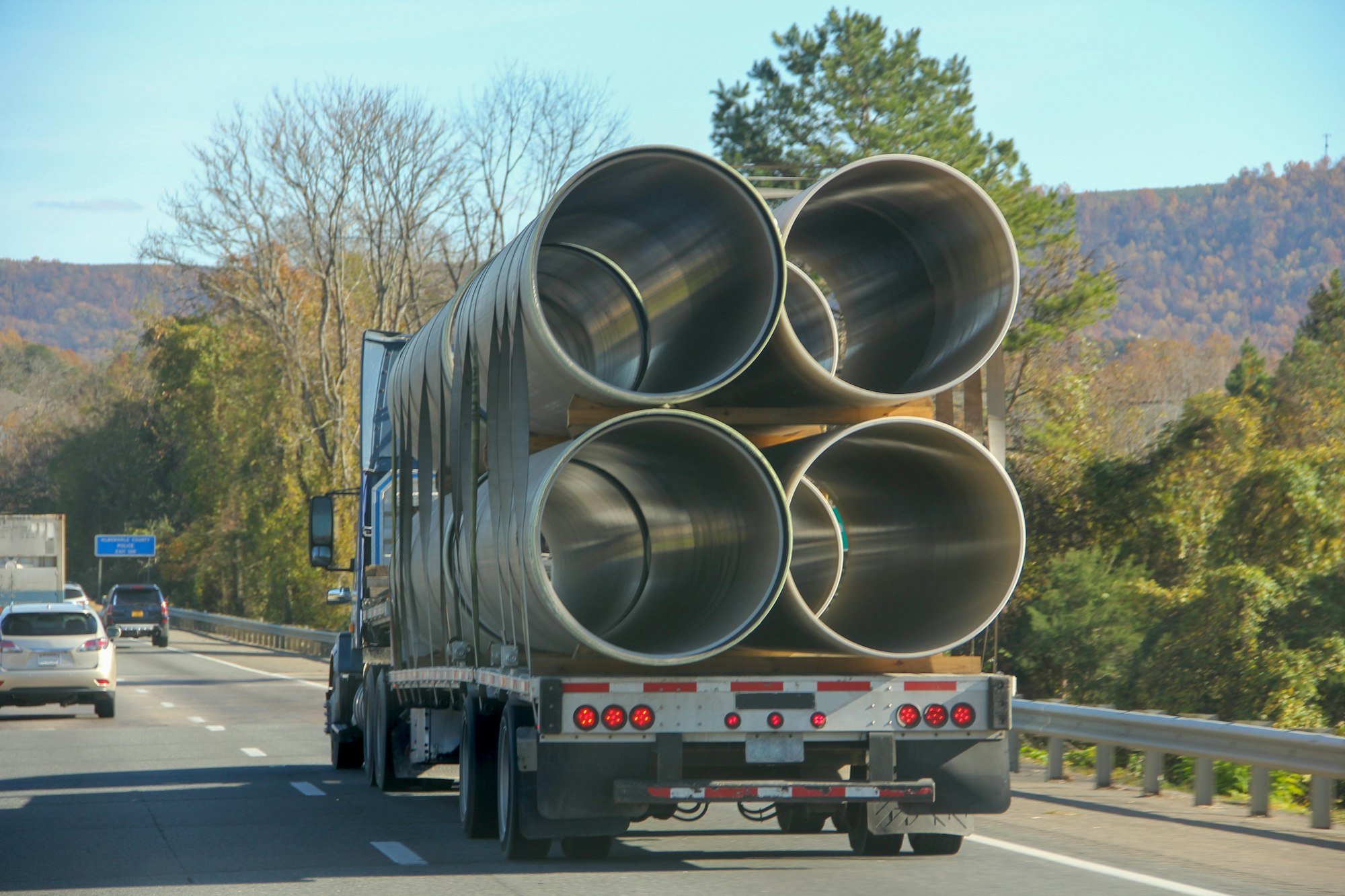 A flatbed truck carrying big size metallic cylinder pipes in the interstate.